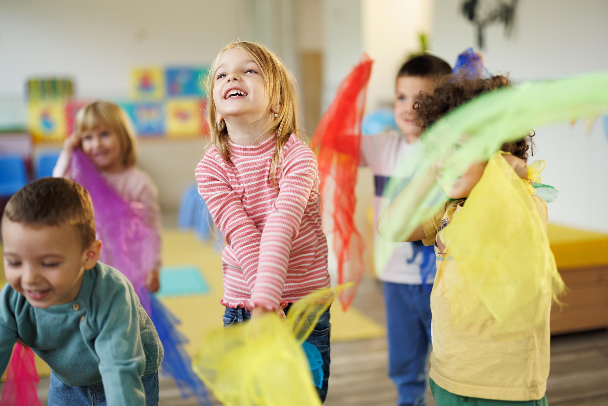 Group of happy children in kindergarten dance with scarves in their hands
